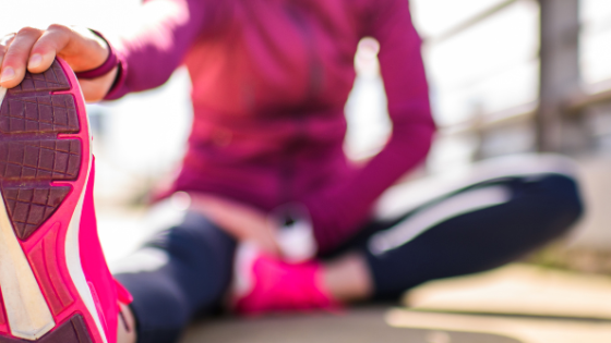 Athlete sitting on the ground, stretching while grabbing one foot
