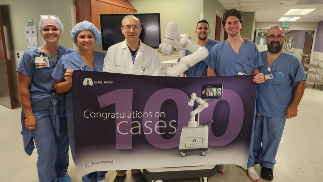 Doctors and nurses standing by a piece of medical equipment holding a banner