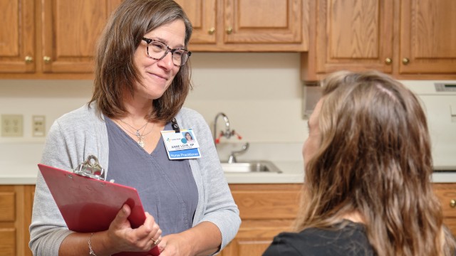 Doctor is standing and holding a clipboard while smiling at a sitting patient