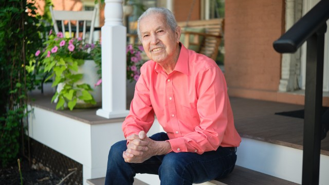 Man sitting on front porch steps smiling with his hands clasped