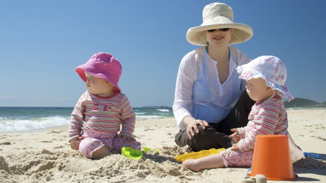Mother and two children sitting on sand at the beach
