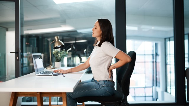 Woman sitting at a desk with her hand on her lower back