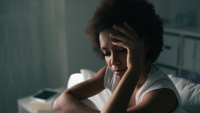 Woman sitting on bed holding her head in her hand