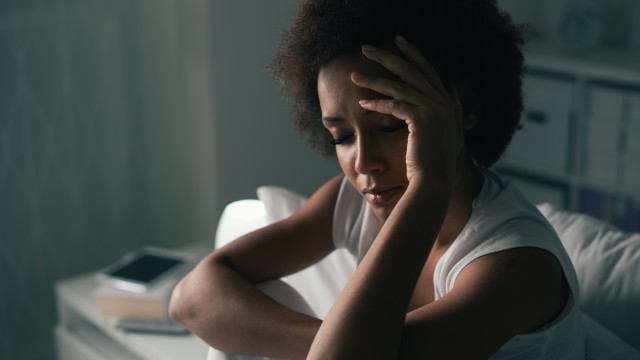Woman sitting on bed holding her head with eyes closed