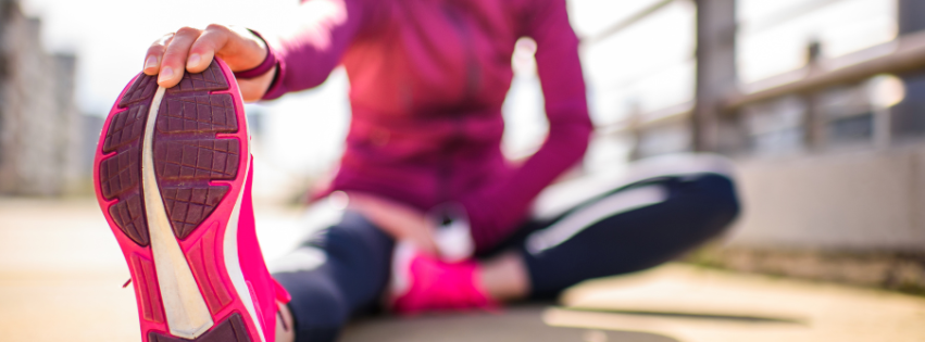 Athlete sitting on the ground, stretching while grabbing one foot