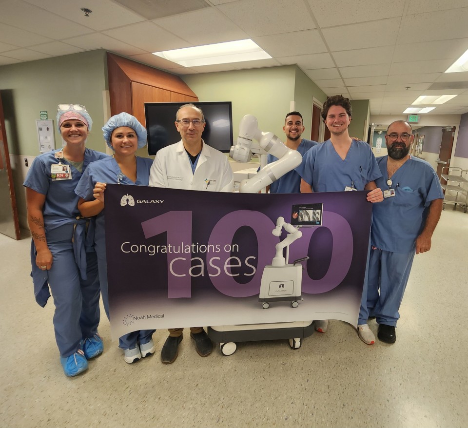 Doctors and nurses standing by a piece of medical equipment holding a banner