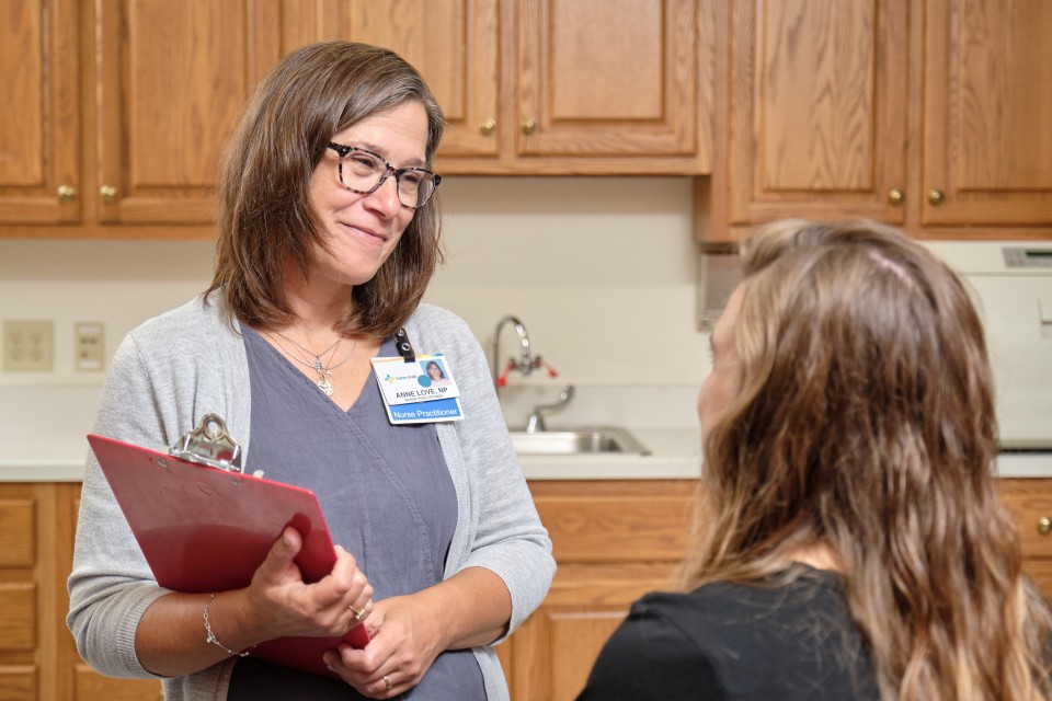 Doctor is standing and holding a clipboard while smiling at a sitting patient