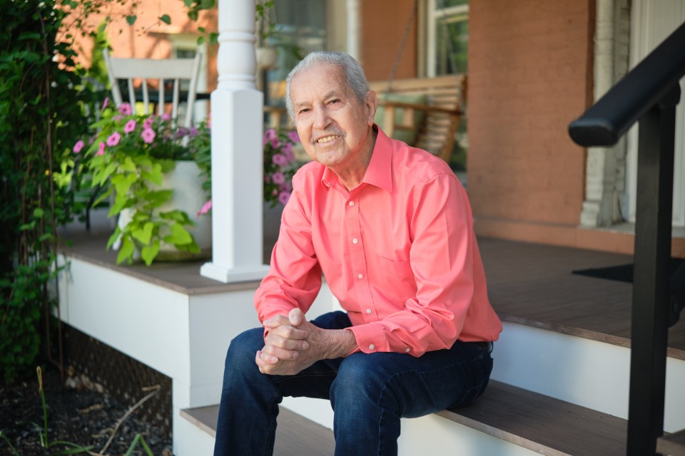 Man sitting on front porch steps smiling with his hands clasped