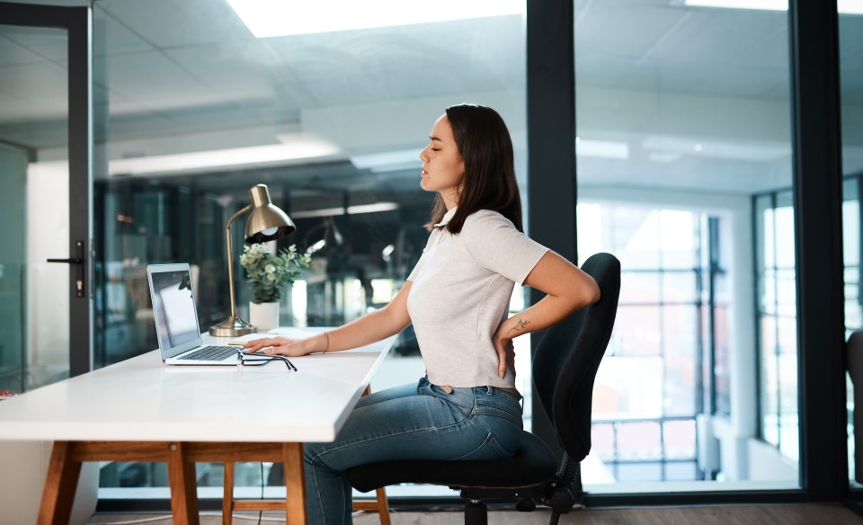 Woman sitting at a desk with her hand on her lower back