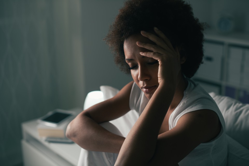 Woman sitting on bed holding her head with eyes closed