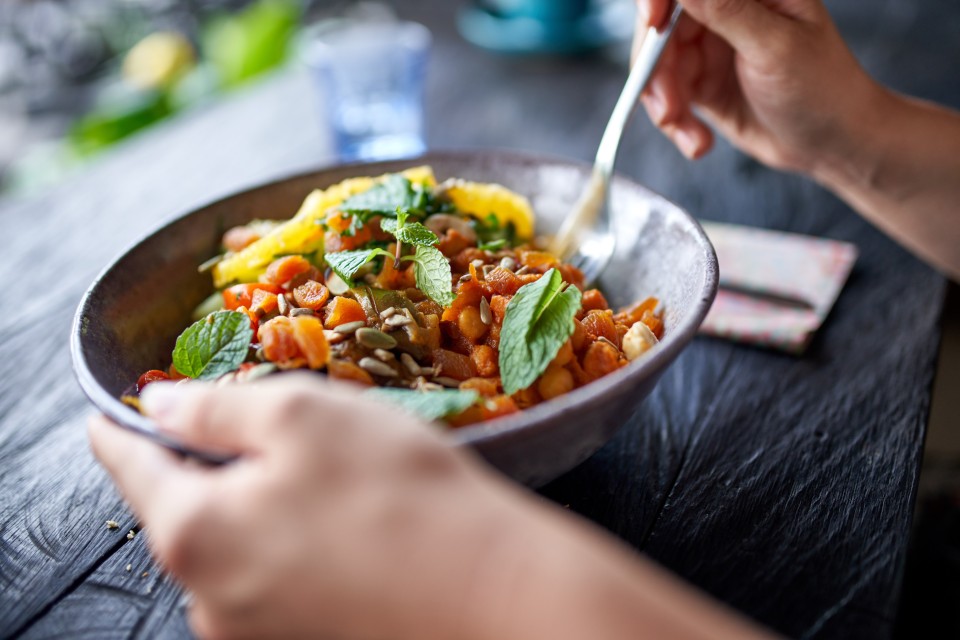 Hands holding a fork and a healthy bowl of salad
