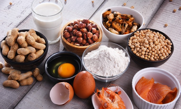 Several bowls of single ingredient foods, a glass of milk and a broken eggshell on the table