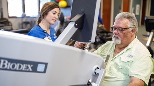 Man sitting at an exercise machine with nurse standing near