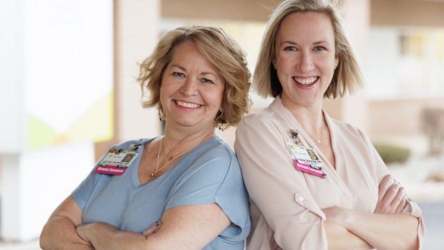 Female breast surgeons smiling while standing back-to-back with arms crossed.