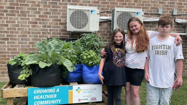 Three people standing to the right of a raised bed garden