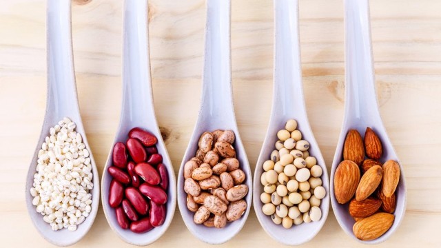 White serving spoons, containing nuts and beans, lined up in a row on a cutting board