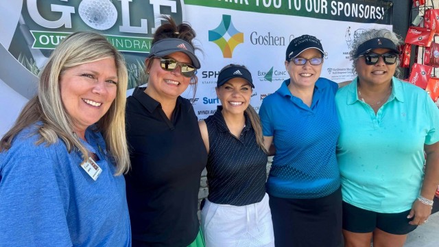 Five women posing in front of a sponsor board