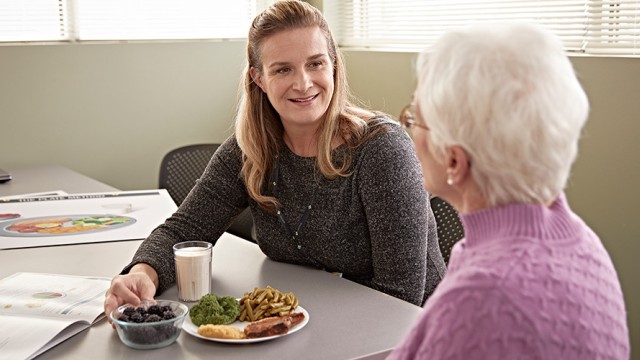 Dietitian sitting at a table while showing a patient food portions on a plate