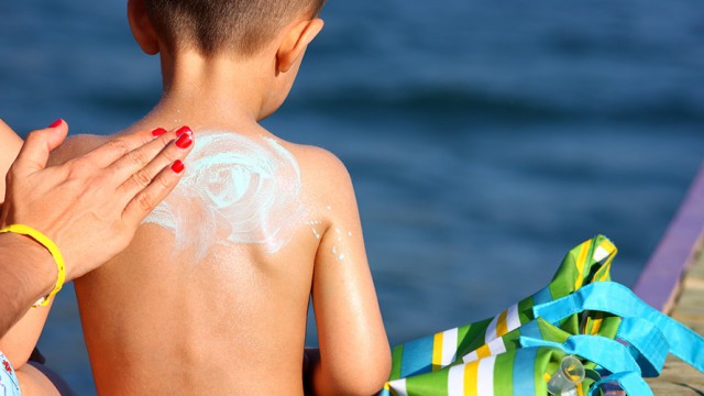 Woman's hand rubbing sunscreen lotion on a small boy's back