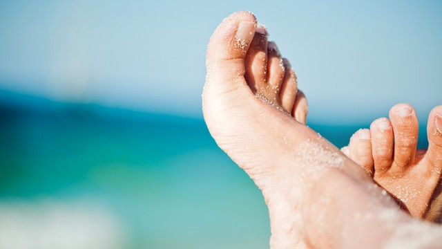 Two sand-covered feet with water in the background