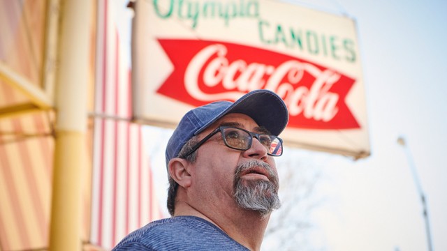 Man with a baseball cap standing in front of a sign