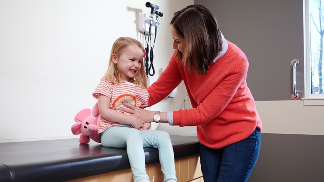 Woman standing with her child who is sitting on an examination table