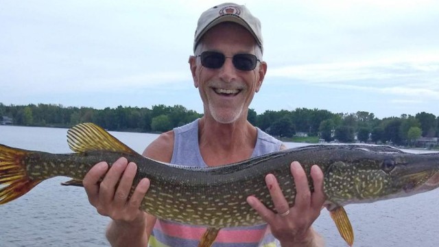 A smiling man proudly holding up a big fish that he caught.