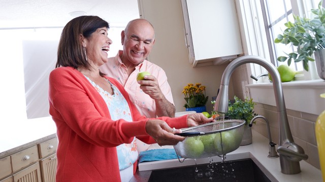 Woman and man standing in a kitchen, laughing while rinsing apples