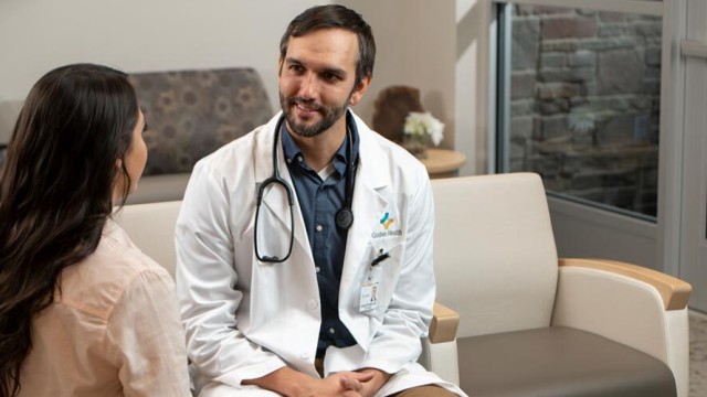 Doctor with a stethoscope around his neck is sitting facing a patient