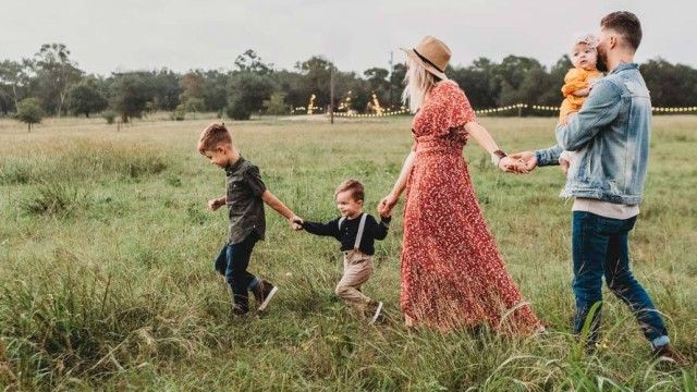 Man and woman with three small children holding hand while walking in a field