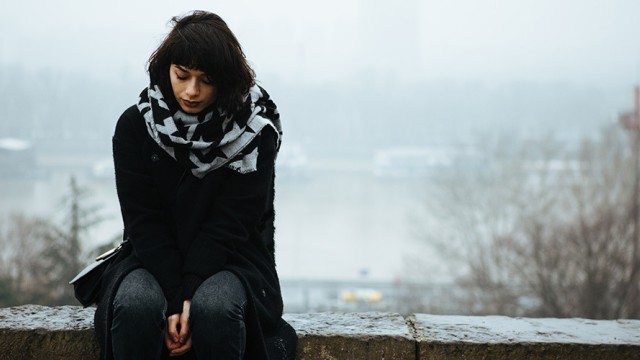 Sad woman sitting on a ledge with a cloudy background