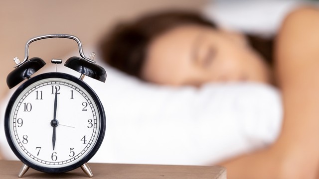 Alarm clock with a woman sleeping on her pillow in the background