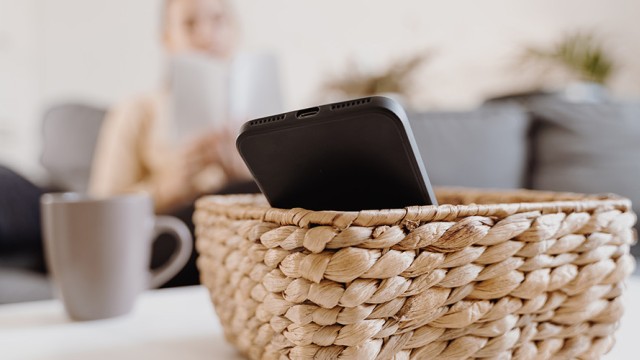 Basket with a phone on a table. A gray mug is in the background.