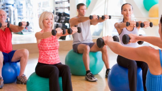 People sitting on a ball with bar bells in their hands