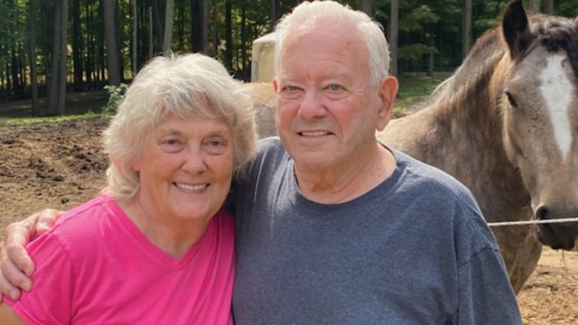 Man with his arm around a woman with horses in the background