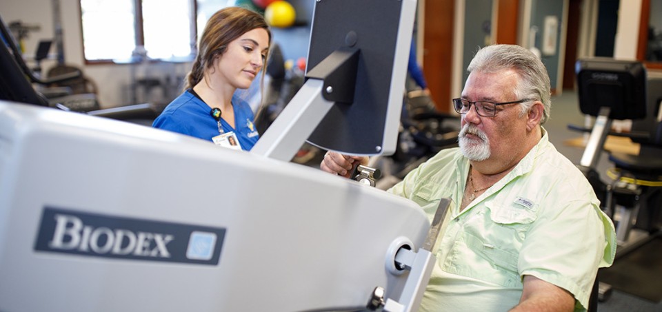 Man sitting at an exercise machine with nurse standing near