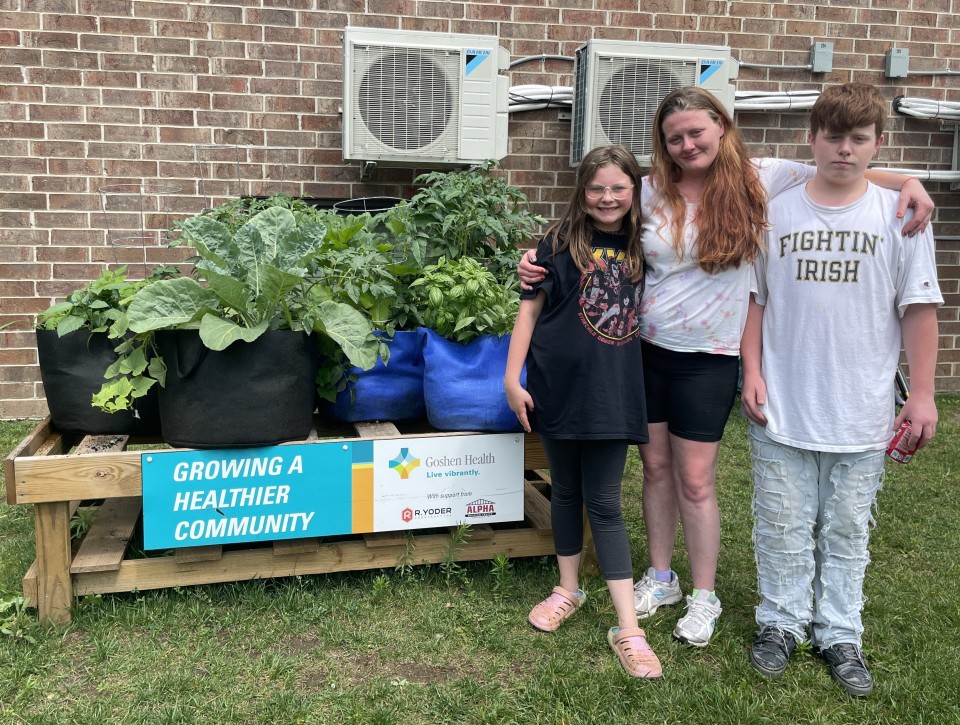 Three people standing to the right of a raised bed garden