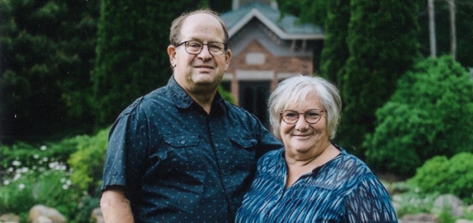 Couple standing shoulder to shoulder with a house and woods in the background