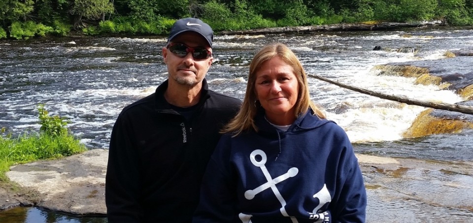 Man and woman standing in front of a short waterfall in a river