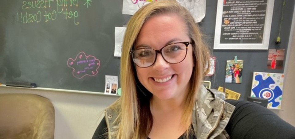 Woman smiling with a classroom chalkboard in the background