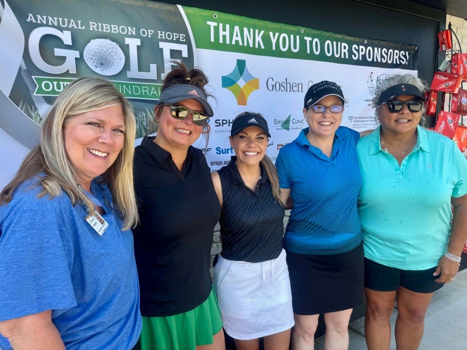 Five women posing in front of a sponsor board