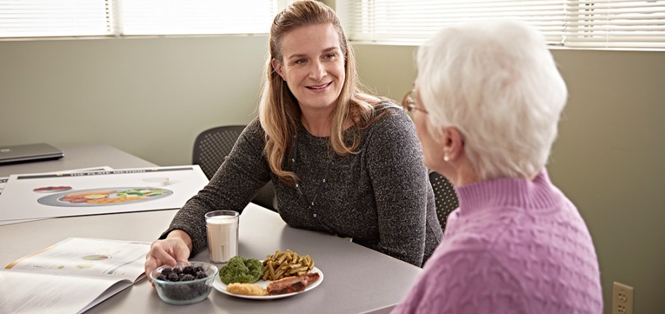 Dietitian sitting at a table while showing a patient food portions on a plate