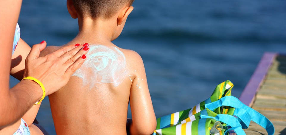 Woman's hand rubbing sunscreen lotion on a small boy's back