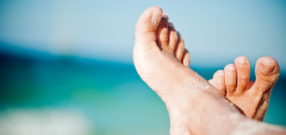 Two sand-covered feet with water in the background