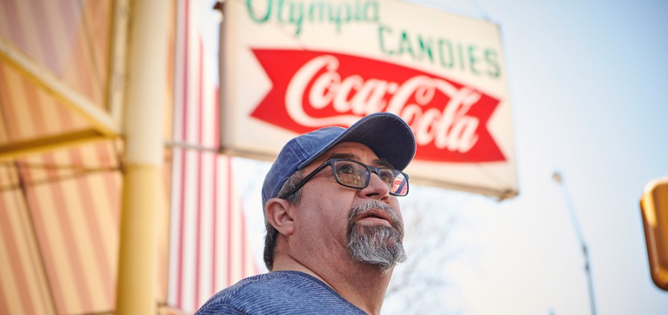Man with a baseball cap standing in front of a sign