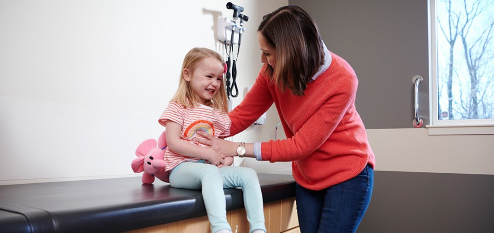Woman standing with her child who is sitting on an examination table