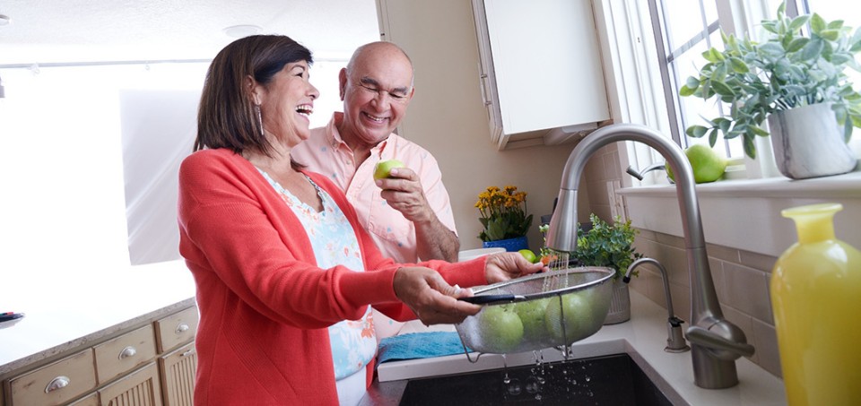 Woman and man standing in a kitchen, laughing while rinsing apples