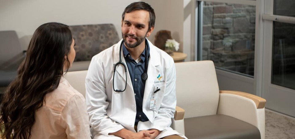 Doctor with a stethoscope around his neck is sitting facing a patient
