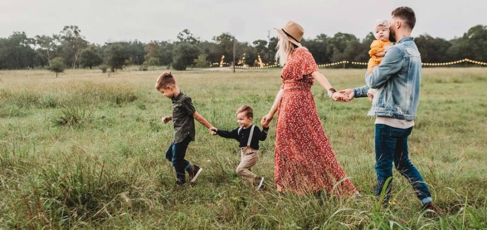 Man and woman with three small children holding hand while walking in a field