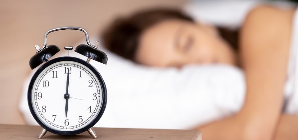 Alarm clock with a woman sleeping on her pillow in the background